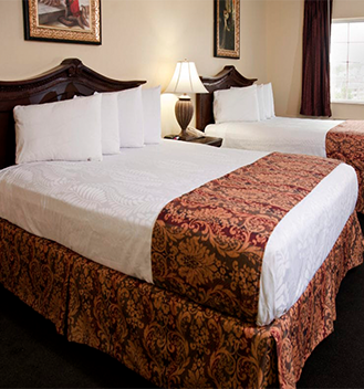 Standard Rooms at the Stone Castle Hotel and Conference Center, Branson, Missouri. Two queen beds with four pillows each, whites sheets and a red regally patterned bed scarf.