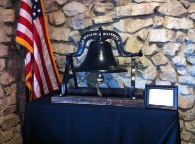 A memorial bell sits proudly by an American Flag.