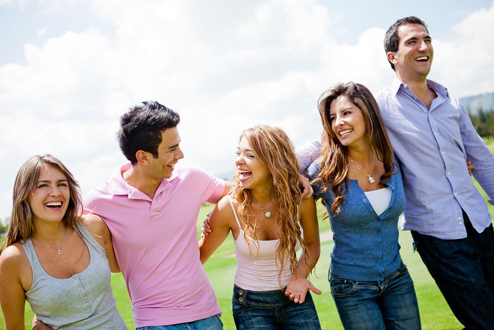 A group of five adult firends is walking on the golf course and laughing happily.