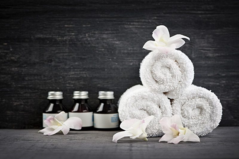 Three white towels are rolled up with white irises around them and three bottles of essential oils lined up beside them.
