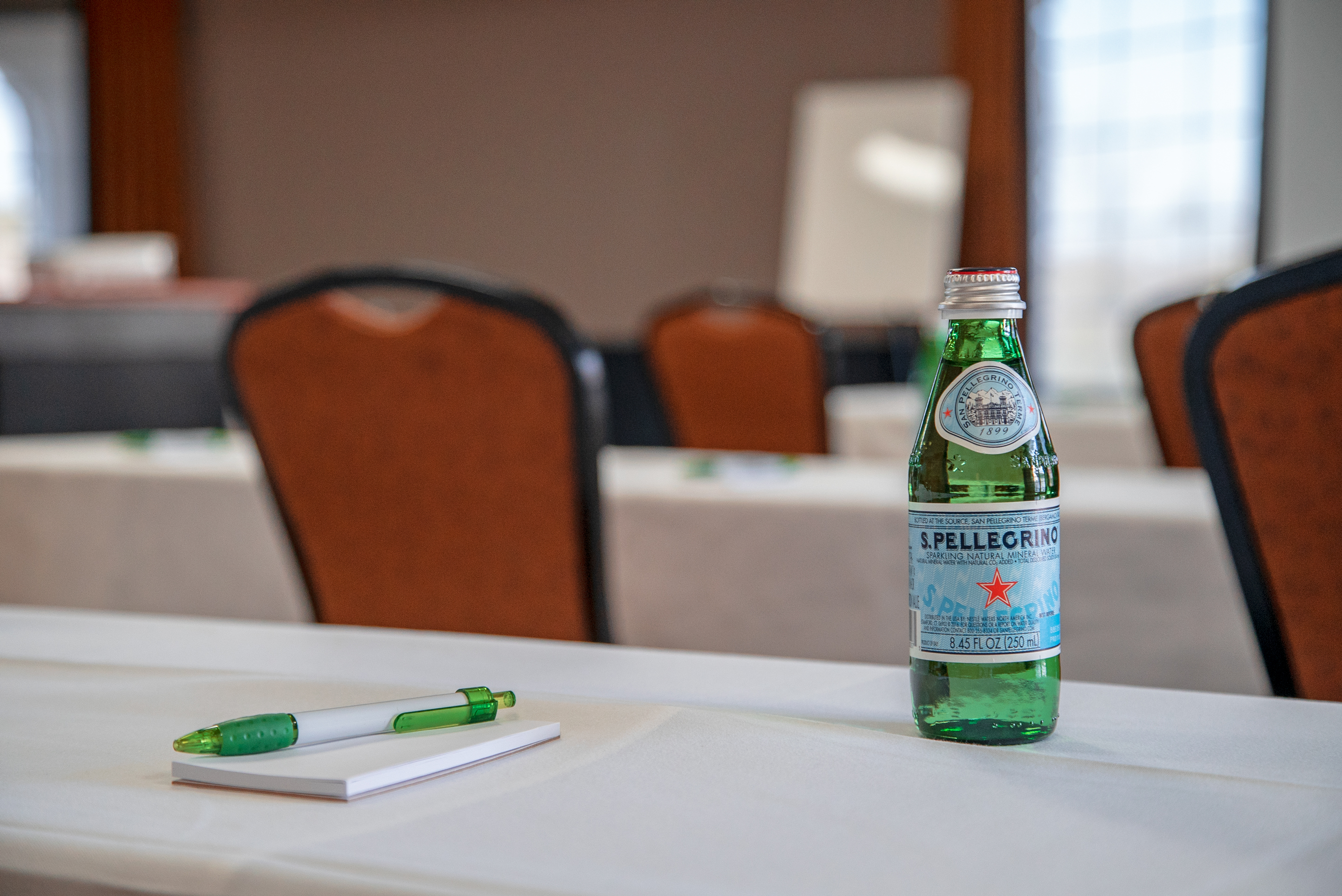 A meeting room with a table, chairs, pen, notepad, and bottle of water.