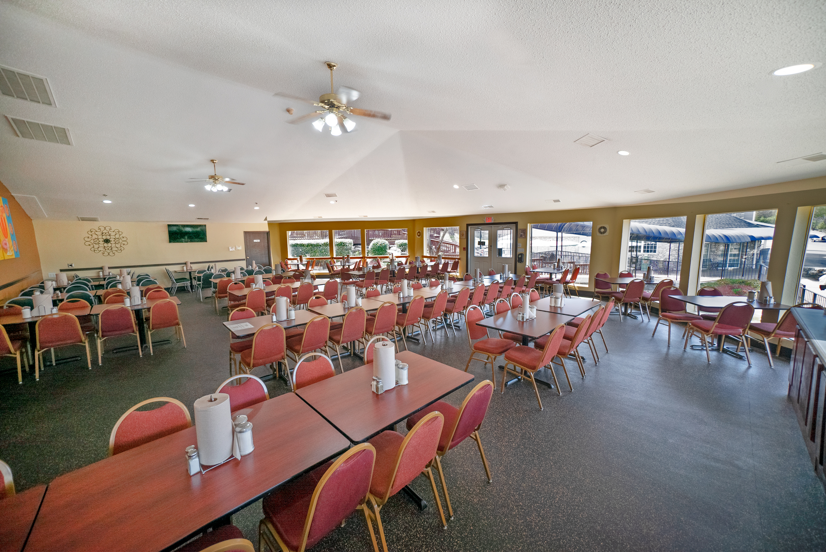 A large dining area with many tables and chairs, ceiling fans, and windows.