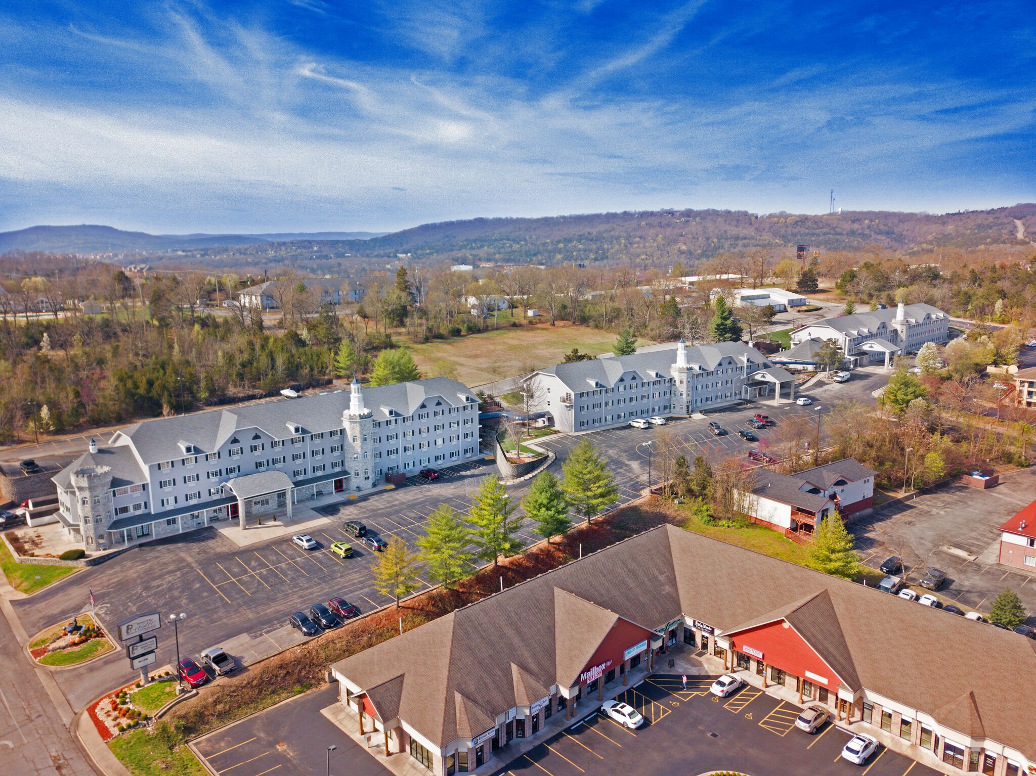 An aerial view of the Stone Castle Hotel and Conference Center with a parking lot and surrounding trees and mountains.