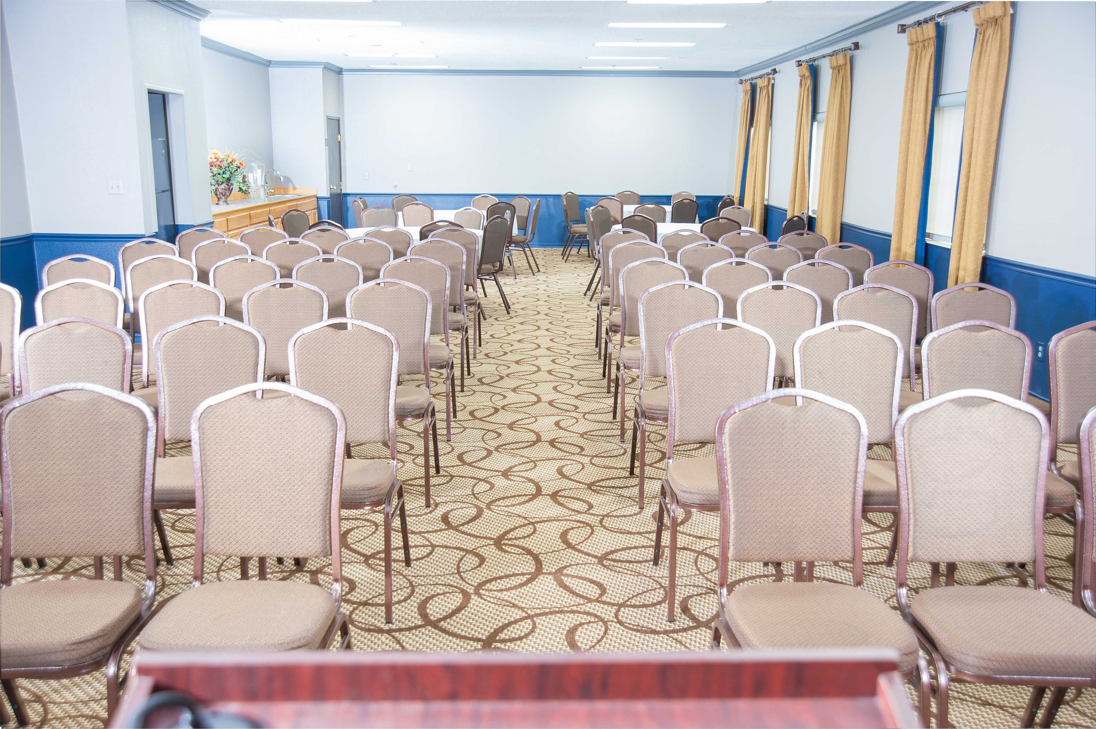 A large meeting room with rows of chairs facing a front area with a table and flowers.