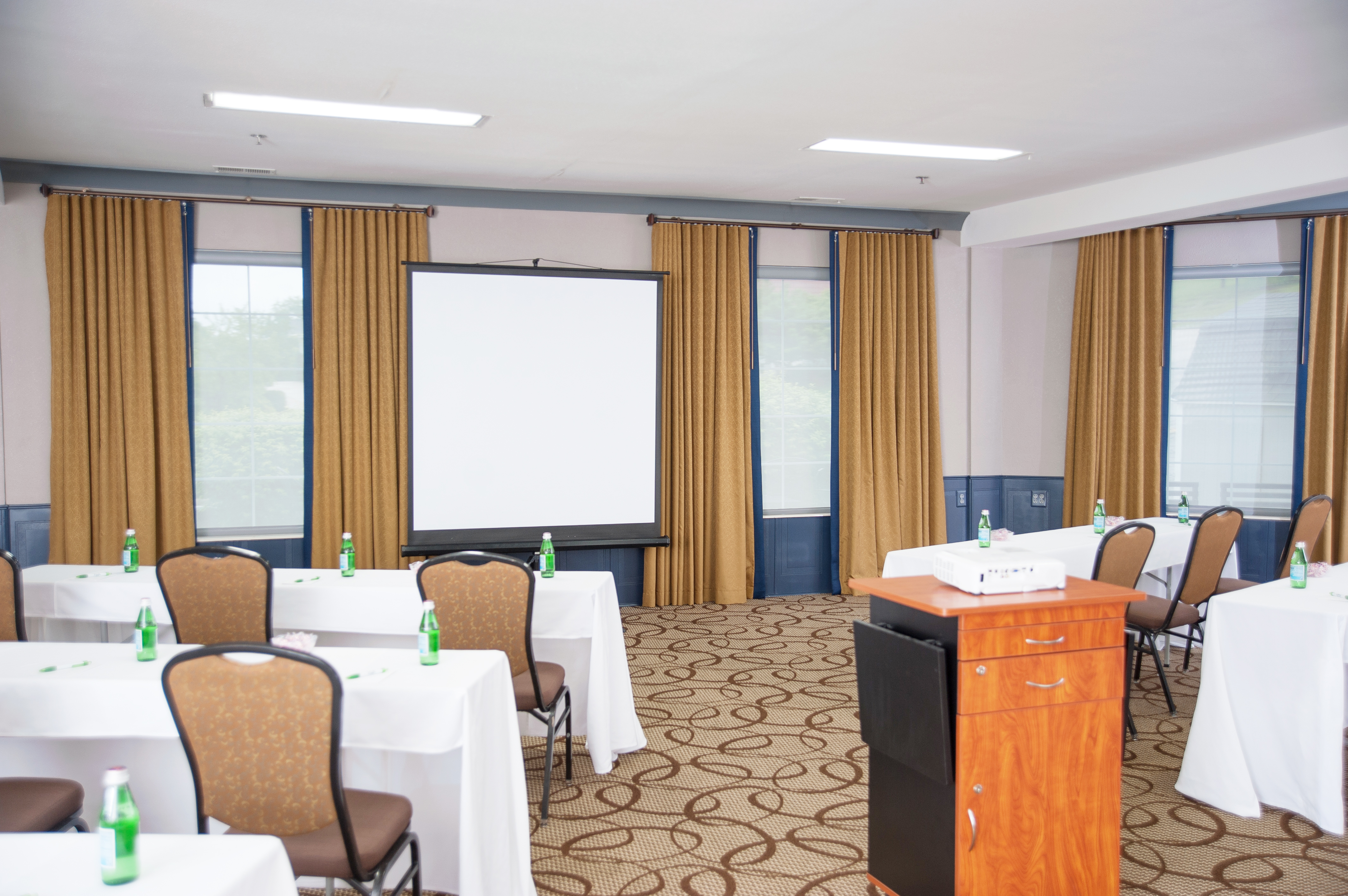 A conference room with tables, chairs, a projector screen, and a podium.